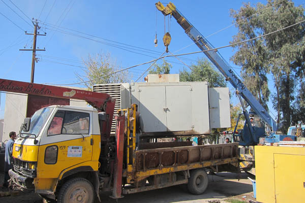 A crane lifts an old generator onto a flatbed truck at Bost Hospital